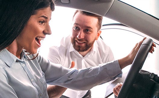 happy woman testing a car with dealer